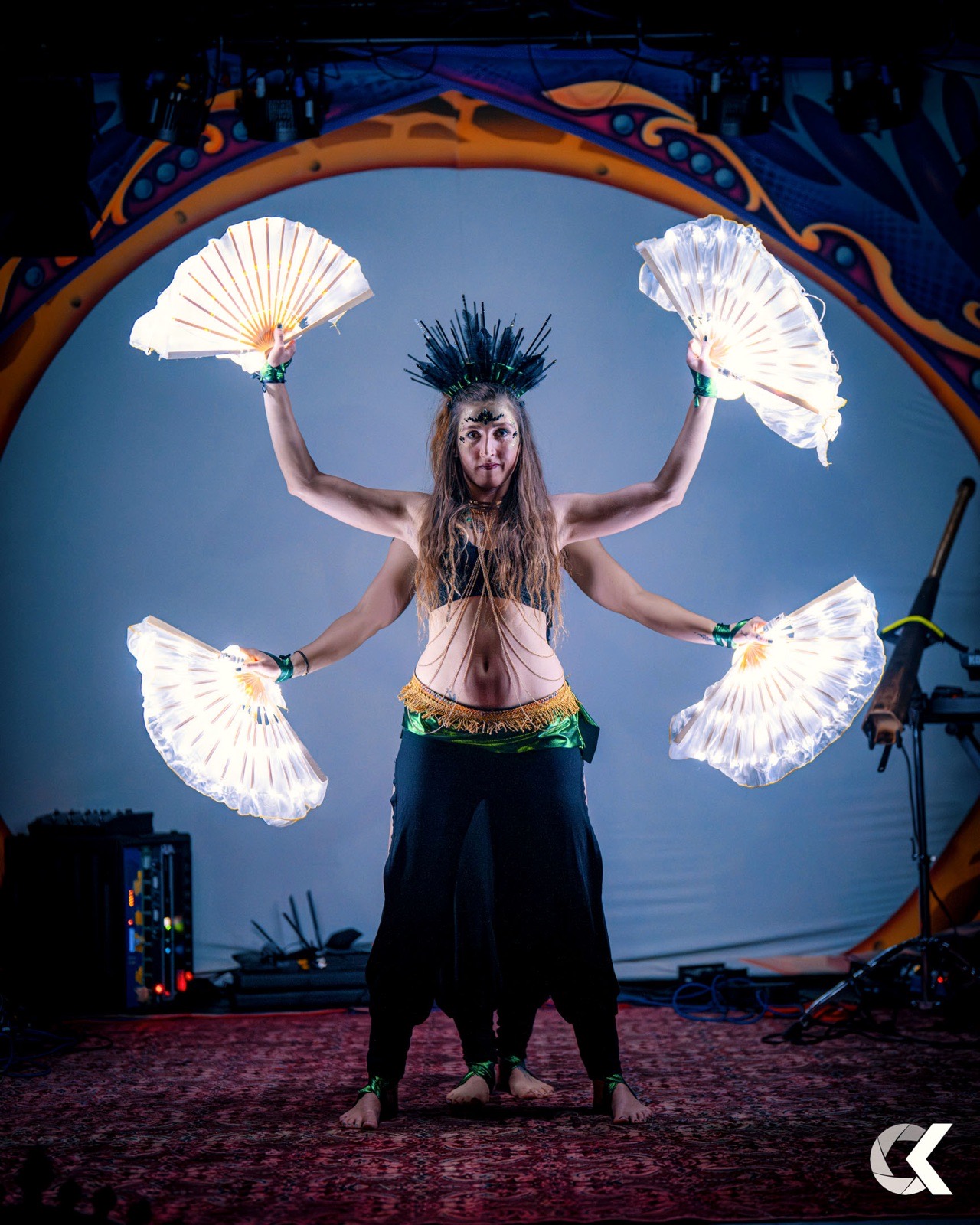 Artistin mit vier leuchtenden LED-Fächern auf bunter Festivalbühne