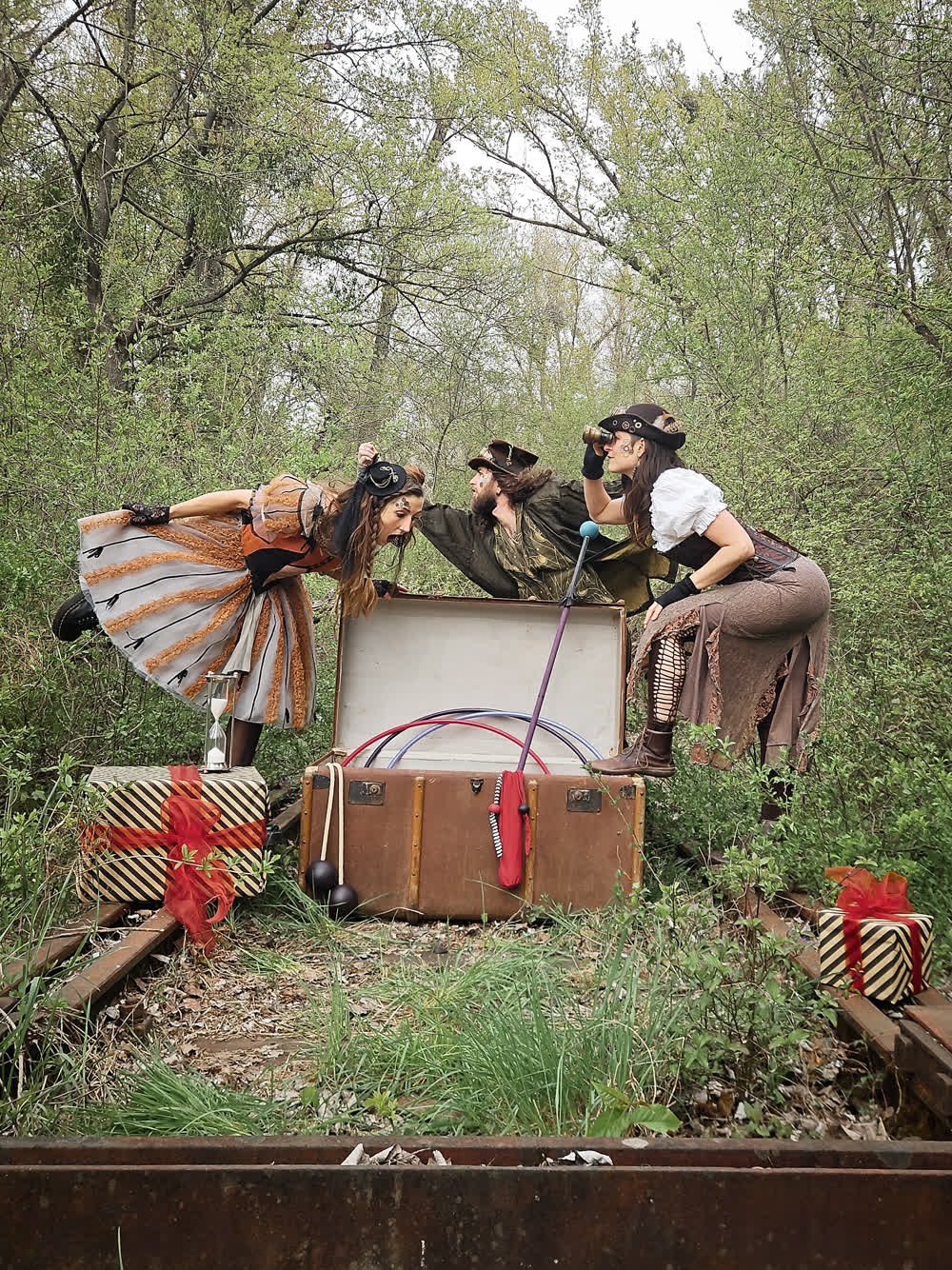 Three steampunk-costumed artists with a trunk, hoops and clubs in woodland