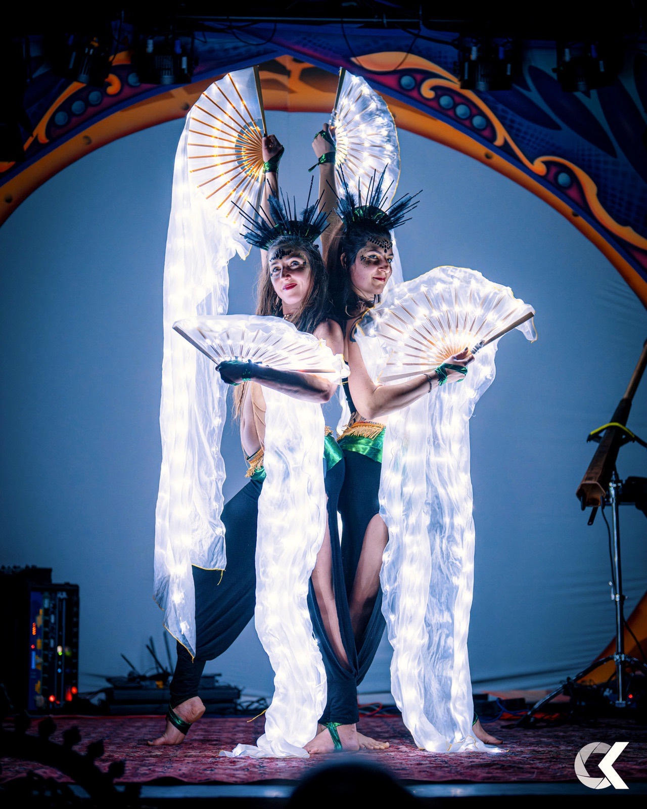 Two dancers with glowing LED fans and feather crowns on stage